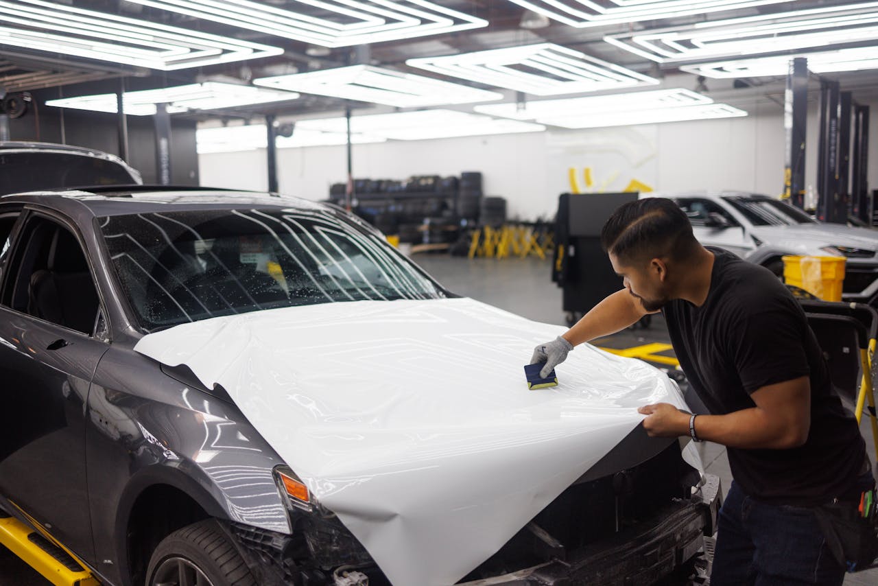 services-03 Man applying vinyl wrap on car hood in an automotive workshop setting.