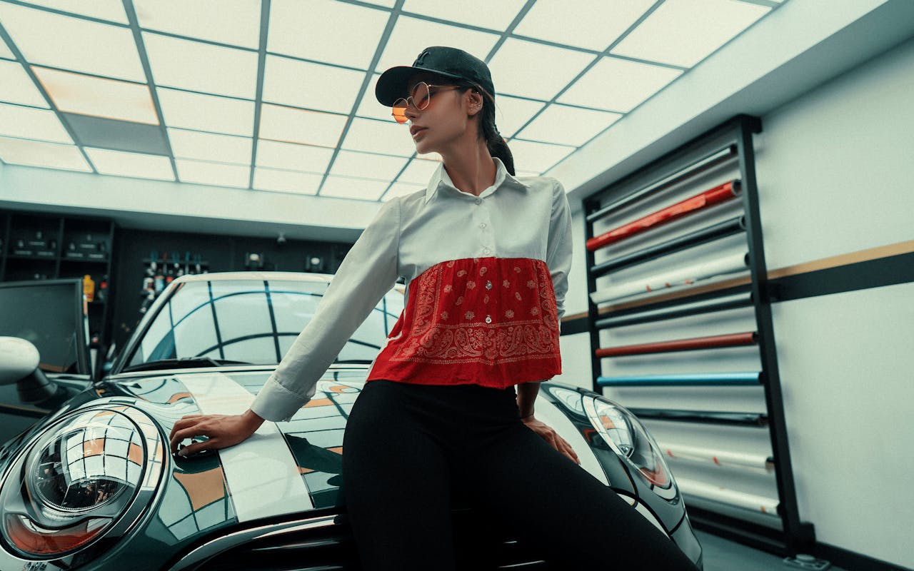 our-journey-02 Fashionable woman posing by a car in a modern garage setting with vibrant lighting.