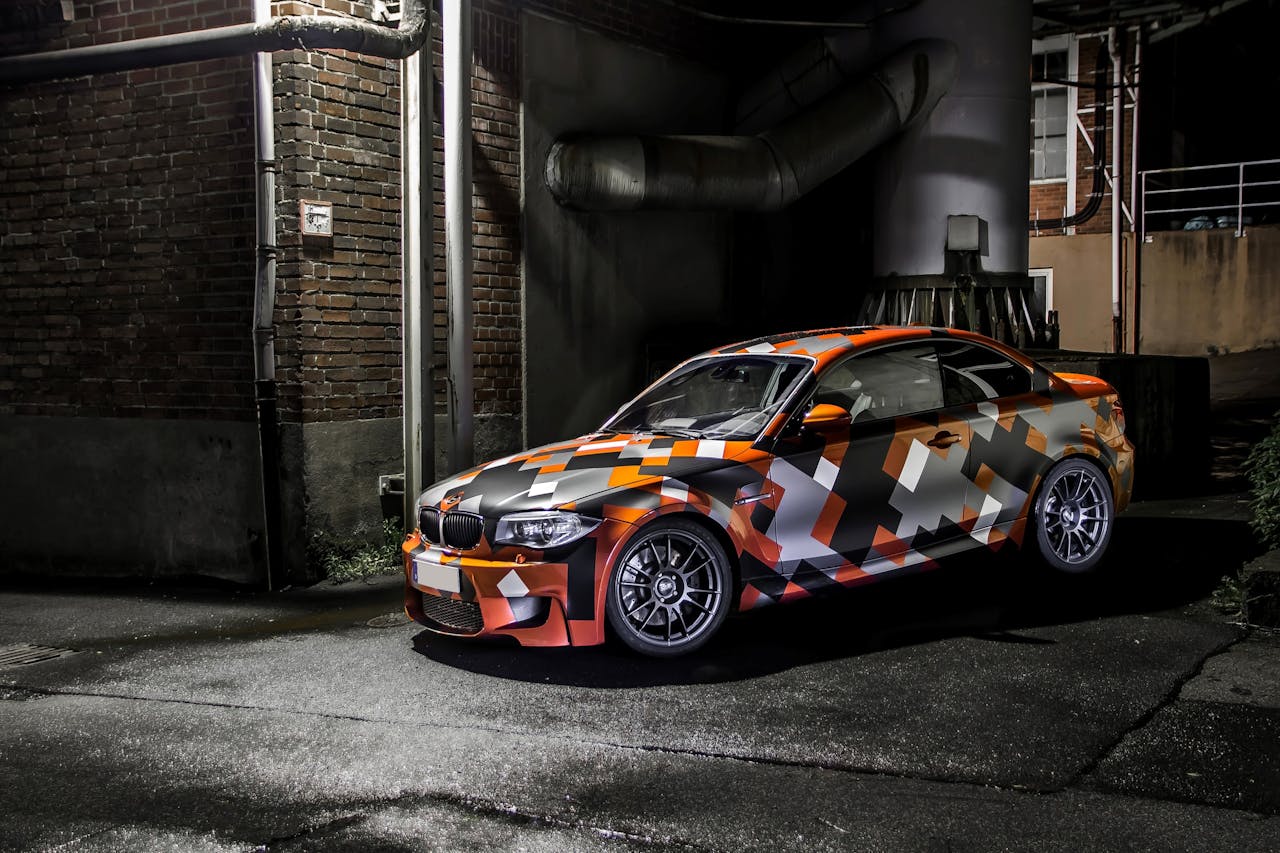 who-we-are Eye-catching camo-wrapped car parked in an industrial area at night, showcasing vibrant colors and sleek design.