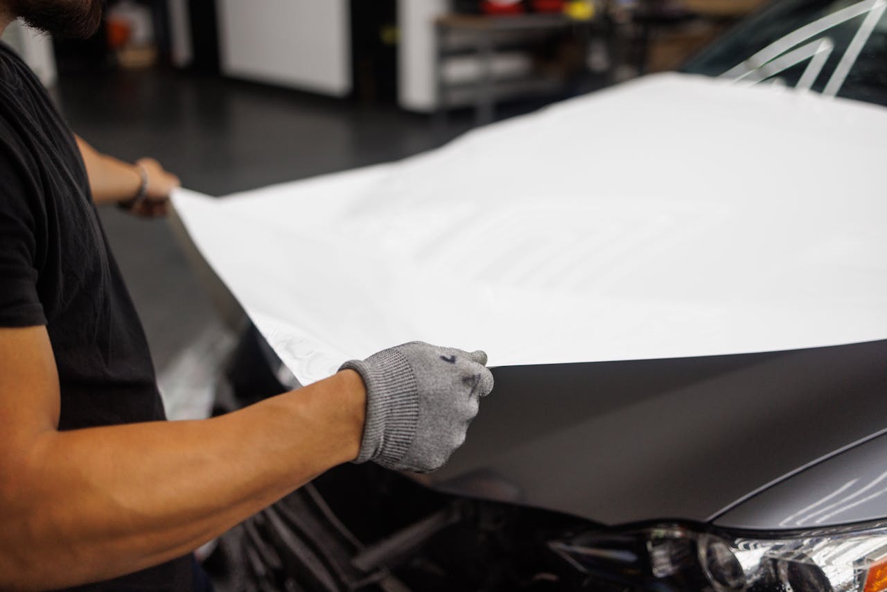 services-04 Person applying vinyl wrap to car hood in garage setting.